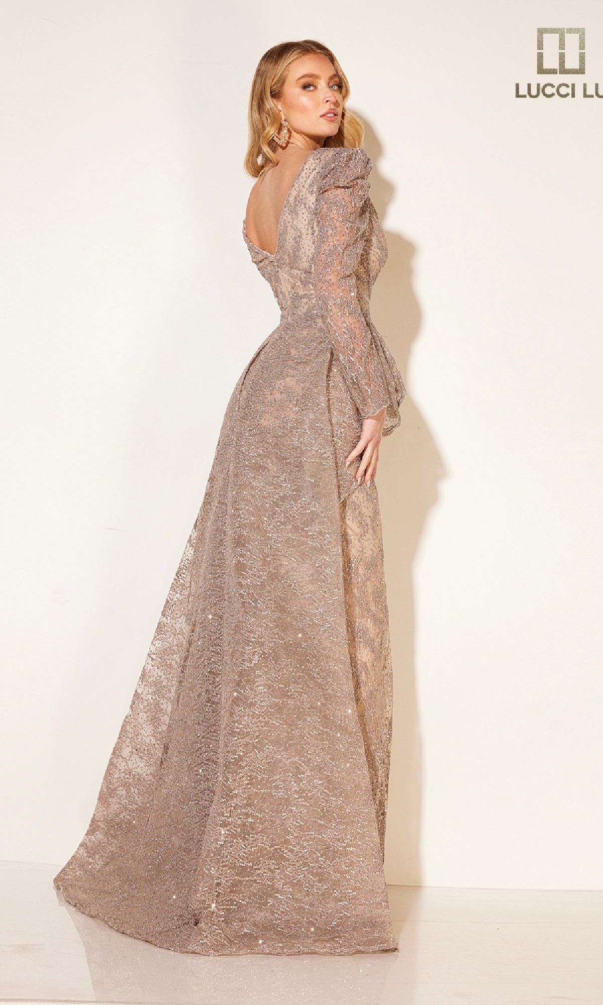 A woman poses in the Lucci Lu C8016 long formal dress, featuring long sleeves and a low back, against a plain light background.